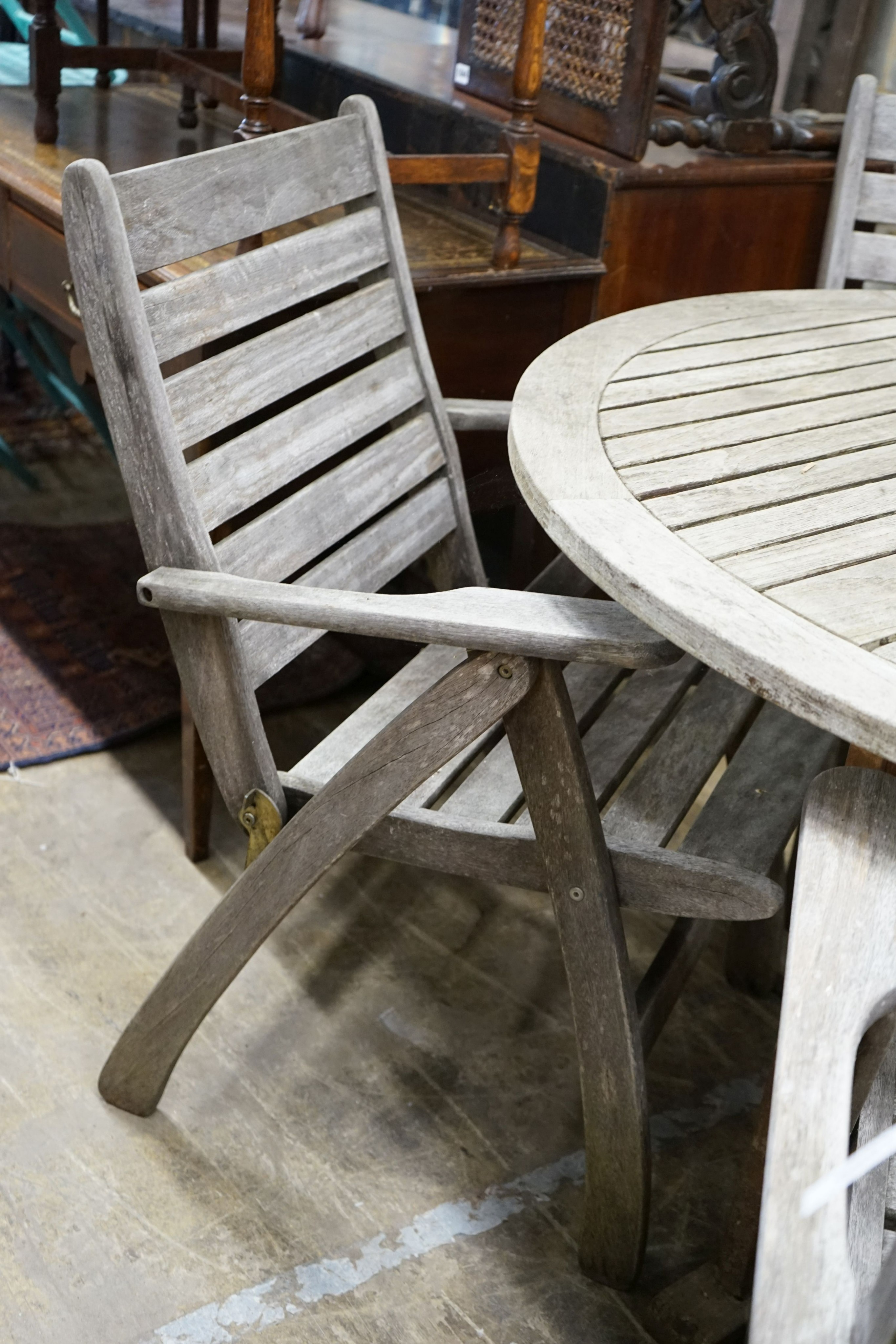 A circular weathered teak slatted garden table, diameter 122cm, height 74cm together with four weathered teak folding garden armchairs